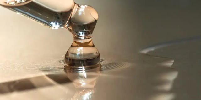 Kropla serum spływające ze szklanej pipety.